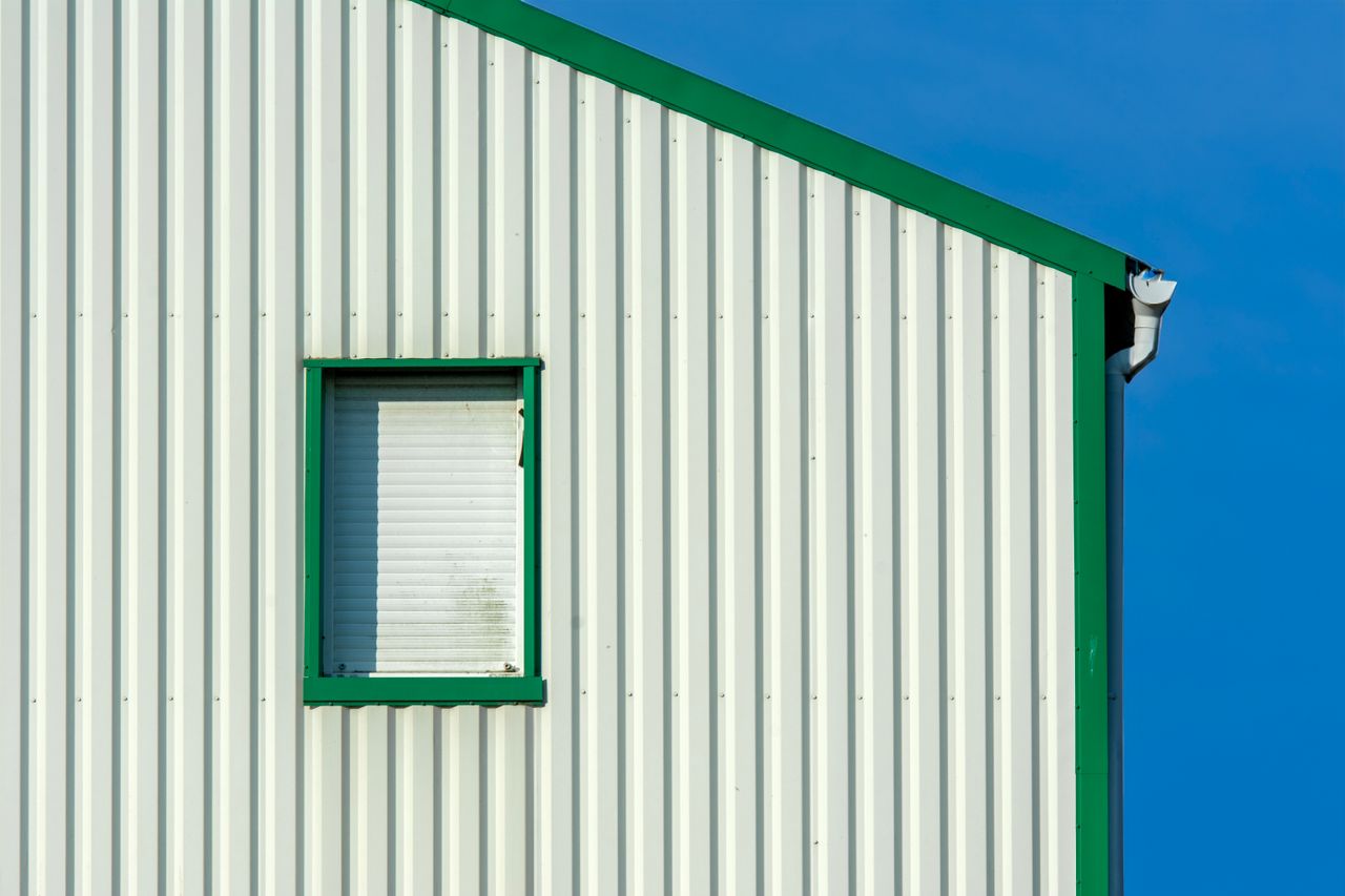 Green-framed window on a white building against a clear blue sky.